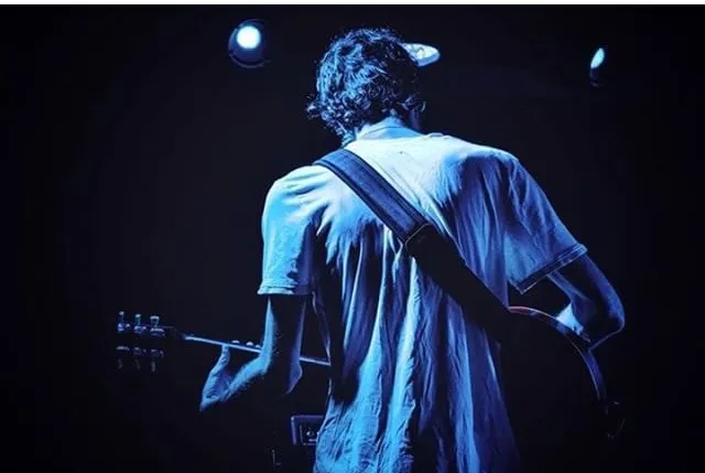 Warren Galea seen from behind during a blue-lit performance