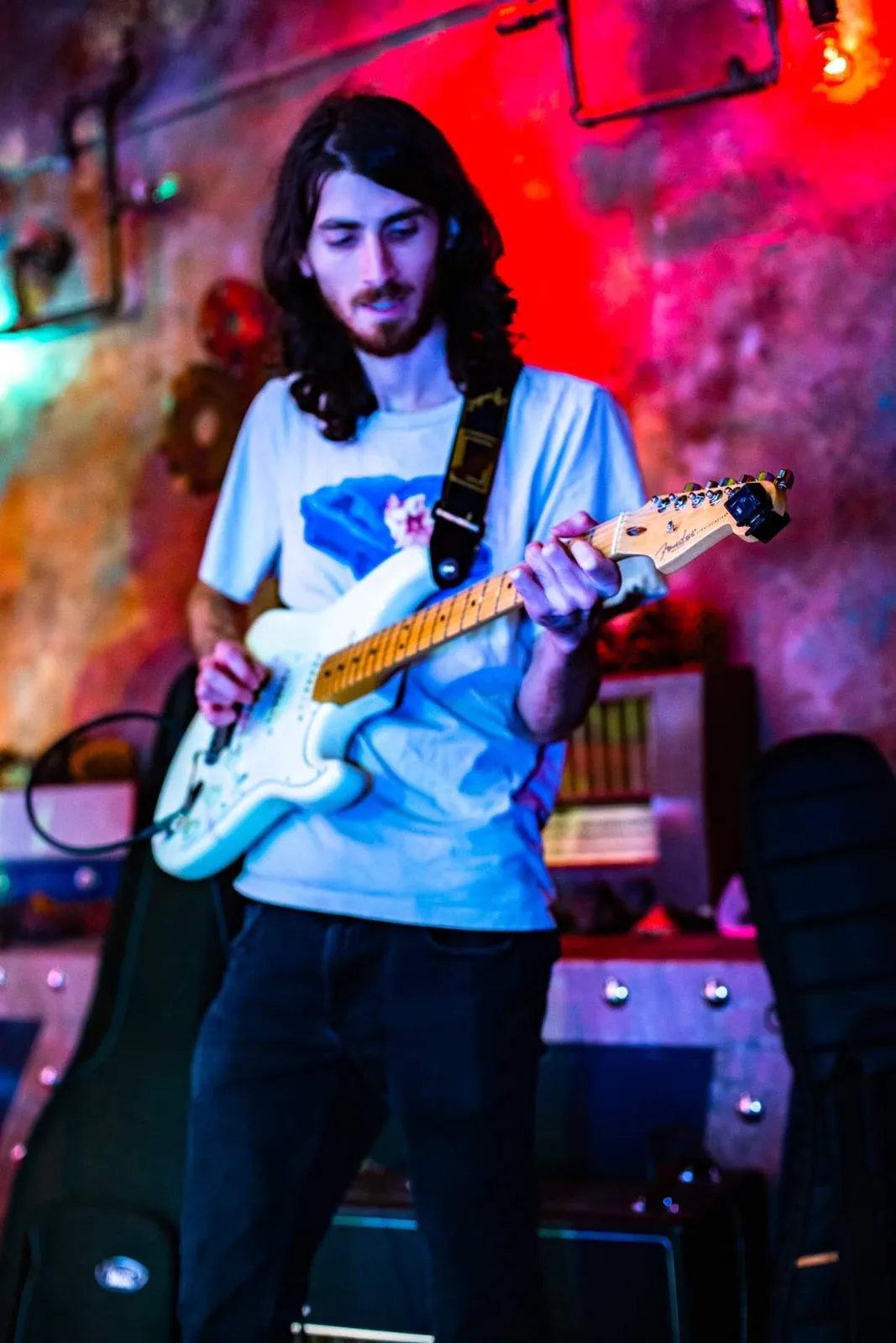 Warren Galea playing a white electric guitar in a red-lit venue