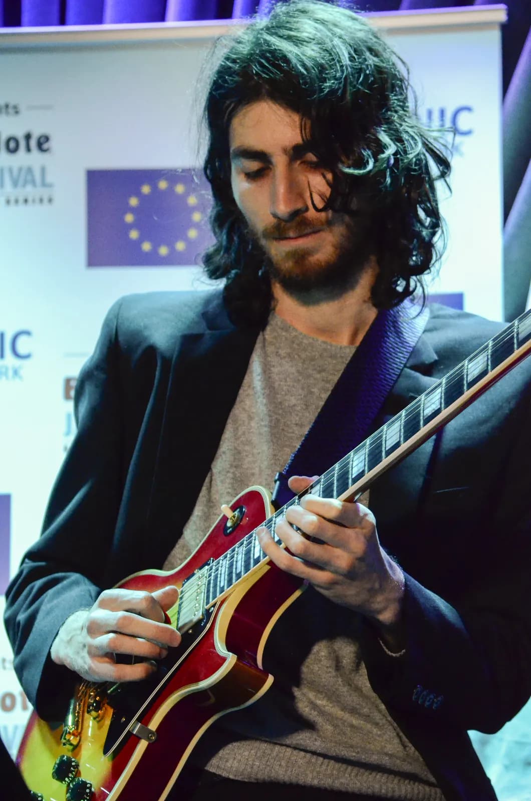 Warren Galea playing guitar at a jazz festival press backdrop